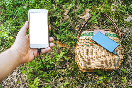 Mockup of a smartphone in a guy's hand. Against the background of the Power Bank and the Gorzina on the groundの写真素材