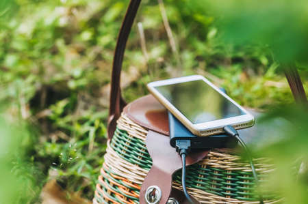 Mock up of a smartphone with charging Power Bank on a basket in the forest. Concept on the theme of outdoor recreationの写真素材