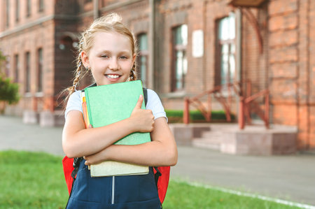 Portrait of a young girl in a school uniform with books in her hands. Against the background of an old collegeの写真素材