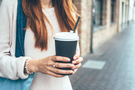The girl holds a paper cup with coffee, on the street in the cityの写真素材