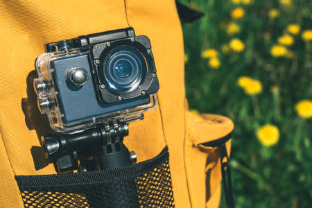 Close-up, action camera in a yellow backpack. Against the background of dandelions on a green fieldの写真素材