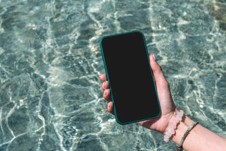 Mock-up, phone in girl's hand. Against the background of waterの写真素材