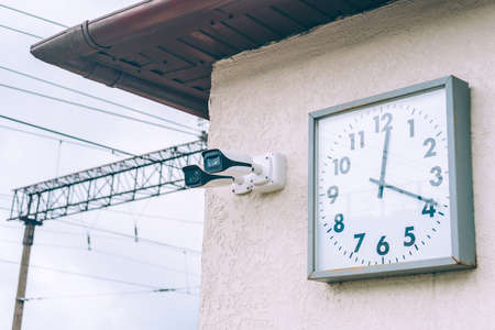 A clock and a security camera are hanging on the wall outside