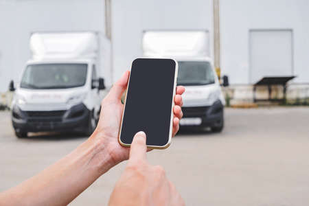 phone in female hands. Against the backdrop of trucks. Logistic conceptの写真素材