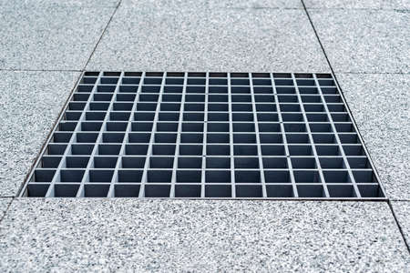 Close-up, metal cover of street water drain. Against the background of paving slabs of gray granite