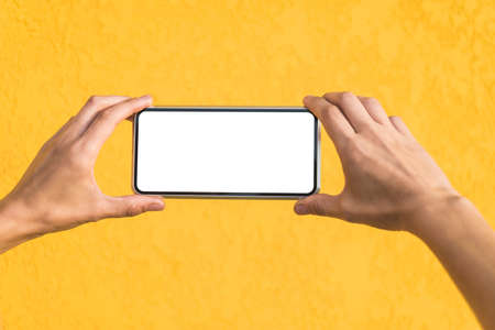 Close-up, Mockup of a smartphone in the hands of a girl. Against the background of a yellow facade made of decorative plasterの写真素材