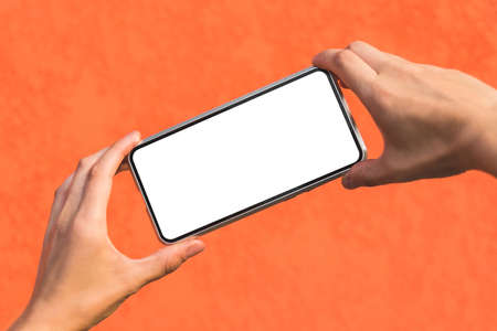 Close-up, Mockup of a smartphone in a girl's hands. Against the background of an orange facade made of decorative plasterの写真素材