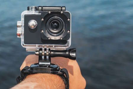 Close-up, Waterproof action camera with mounts on a man's hand. Against the backdrop of the blue water of the seaの写真素材