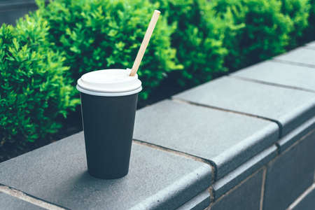 Close-up, black paper cup of coffee on the street in the cityの写真素材