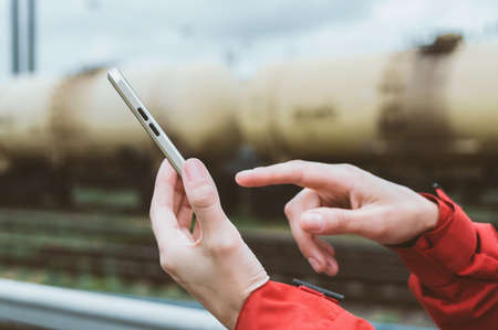 close-up. Finger in front of a smartphone in a man's hand. Against the background of railway cars with oil products tanksの写真素材