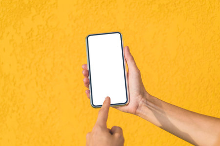 Finger in front of a mockup of a smartphone in a girl's hand. Against the background of a yellow facade made of decorative plaster. close-upの写真素材