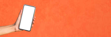 Close-up, Mockup of a smartphone in a girl's hand. Against the background of an orange facade made...