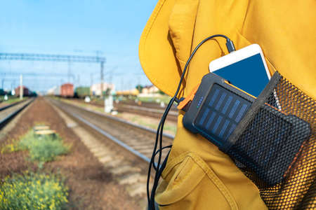 Close-up, a phone with a power bank in a yellow backpack. On the background of the railwayの写真素材