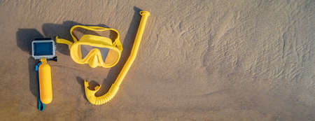 Banner, yellow waterproof action camera with underwater mask and diving snorkel in the water on the seashore with sandy bottom. summer beach holiday conceptの写真素材