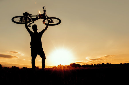 Silhouette of a bicycle over a man's head at sunsetの写真素材