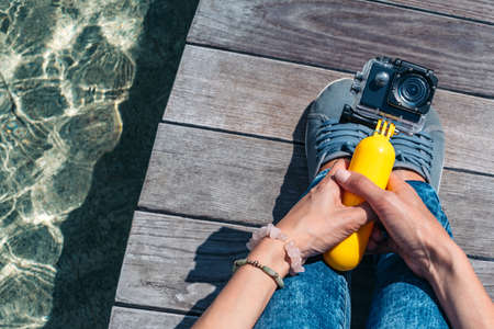 Action camera in the hands of a girl. Against the backdrop of a wooden deck, a tabletop on the surface of the water against the background of the poolの写真素材