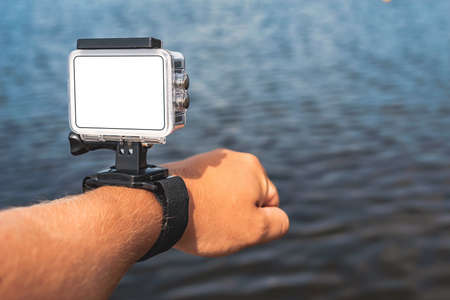 Close-up, mockup of a waterproof action camera with mounts on a man's hand. Against the backdrop of the blue water of the seaの写真素材