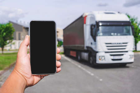 Phone in a man's hand. Against the backdrop of a truck. Logistic conceptの写真素材