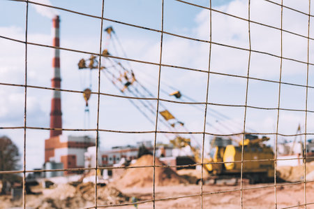Close-up focus on the fence lattice in the foreground. Construction site background, with crane and plantの写真素材