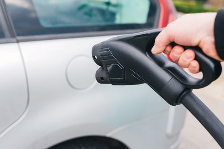 car charger in the hands of a man against the background of a power station for charging cars in an open parking lotの写真素材