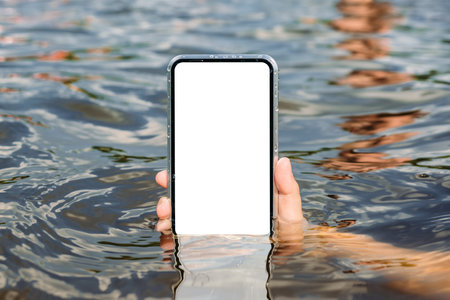 Smartphone mockup with reflections in the water in a man's hand. Against the backdrop of the beach with blue skies. Time for rest and travelの写真素材