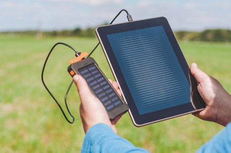 Touch screen of a digital tablet, in the hands of a man there is a power bank charger. Green lawn...