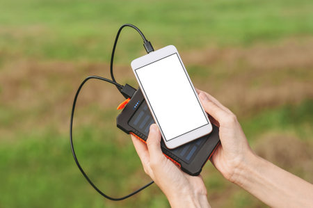 Mockup of a smartphone mobile phone in the hands of a girl with a Power Bank charger. Background of green grass and natureの写真素材