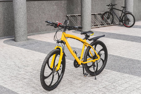 The yellow bicycle is parked on a paved sidewalk on the city street. Side view