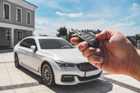 Close-up of a man opening a car with a key fob. Background of a white car parked in a car park near a buildingの写真素材