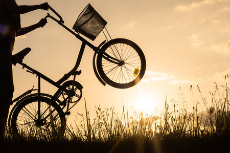 Close-up silhouette of a cyclist woman holding and standing on the back wheel of a bicycle or bike. Sunset backgroundの写真素材