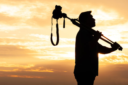 A dramatic silhouette of a man carrying a tripod-mounted camera on his shoulder during a vibrant...