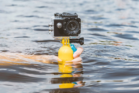 Close-up of a black action camera with a waterproof body, a girl underwater holds her hand on a yellow float. Water background with waves. Photo and video technologies while swimming.の写真素材