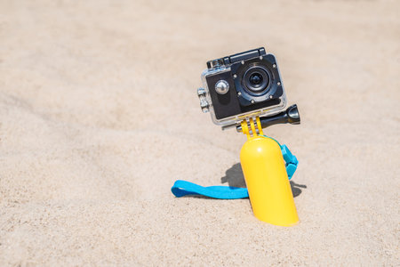 Close-up action camera lens with waterproof body standing on sandy beach with yellow swimming float. sand backgroundの写真素材