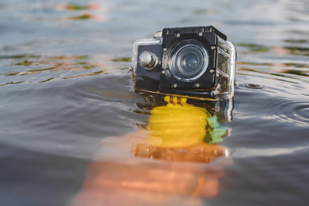 Action camera with a waterproof case in a person's hand over water close-up