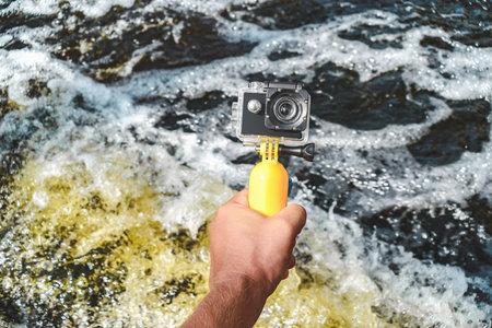 Close-up action camera in a man's hand against the background of water with wavesの写真素材