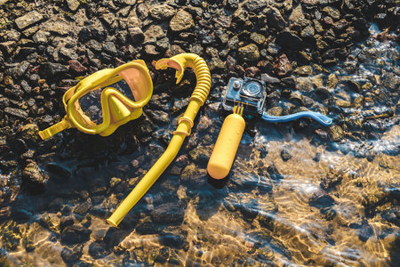 A waterproof action camera with a diving mask and snorkel lies on a rocky shore with water. Time relaxの写真素材
