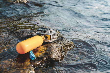An action camera with a yellow float for swimming lies on a stone in the water. Swimming ban conceptの写真素材