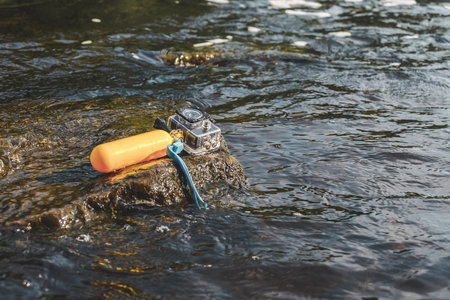 An action camera with a waterproof body and a float for swimming rests on a rock in water with a strong currentの写真素材
