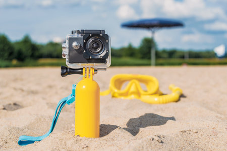 Close-up action camera stands in the sand on a sandy beach. Against the background of a mask with a snorkel and a sky with cloudsの写真素材