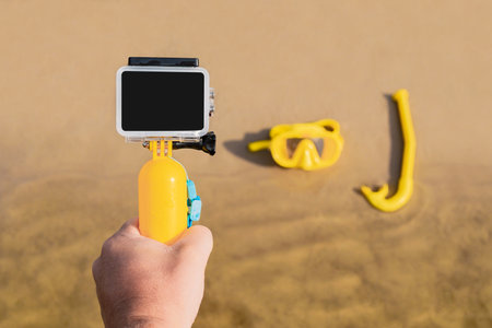 In the man's hand is an action camera close-up. Against the background of a mask and a tube. on the sandy beachの写真素材
