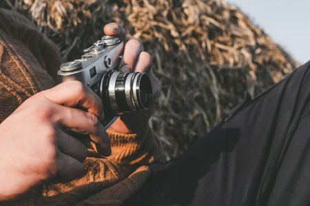 A man holds a vintage camera in his hands. Background close-up of a pile of hay balesの写真素材