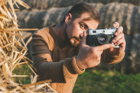 A man takes pictures on a retro camera outdoors. Against the background of large bales of hay
