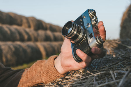 Close-up of a retro camera in a man's hand, photographing a selfie. Hay bale backgroundの写真素材