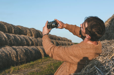 Retro camera in a man's hands, photographing a selfie. Hay bale backgroundの写真素材