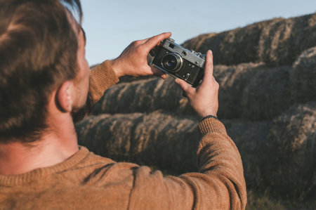 Close-up of a retro camera in a man's hands, photographing a selfie. Hay bale background