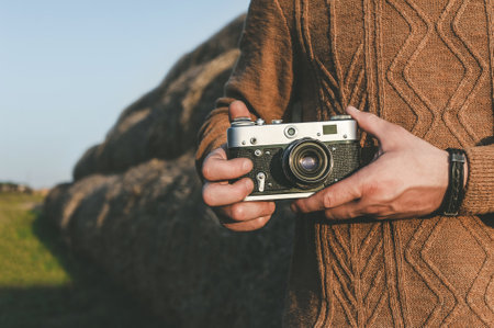 Close-up man holding a retro camera in his hands. Background of a large pile of hay balesの写真素材