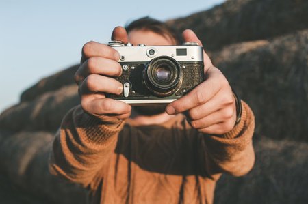 Close-up, A man takes pictures with two hands on a retro camera in a rural area against the background of haystacksの写真素材
