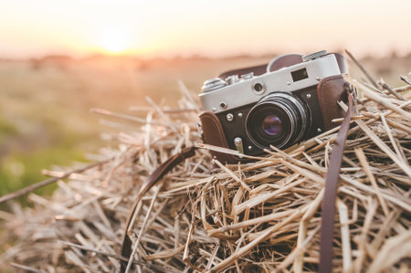 A retro camera lies on a haystack in a field against the background of a sunsetの写真素材