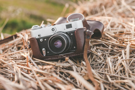 Close-up. A retro camera with a brown case lies on a haystack. Background of a field with green grass, at sunsetの写真素材