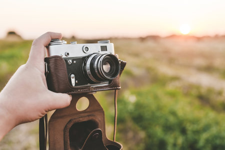 Close-up. Retro camera in a man's hand. Background in the field with sunsetの写真素材